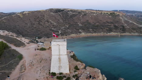 Steinturm-Mit-Der-Flagge-Des-Malteserritters-über-Einer-Bucht,-Antenne