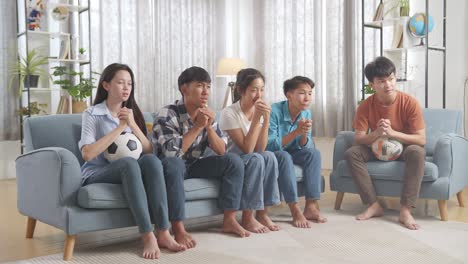 asian teenagers cheering and watching football game on tv at home