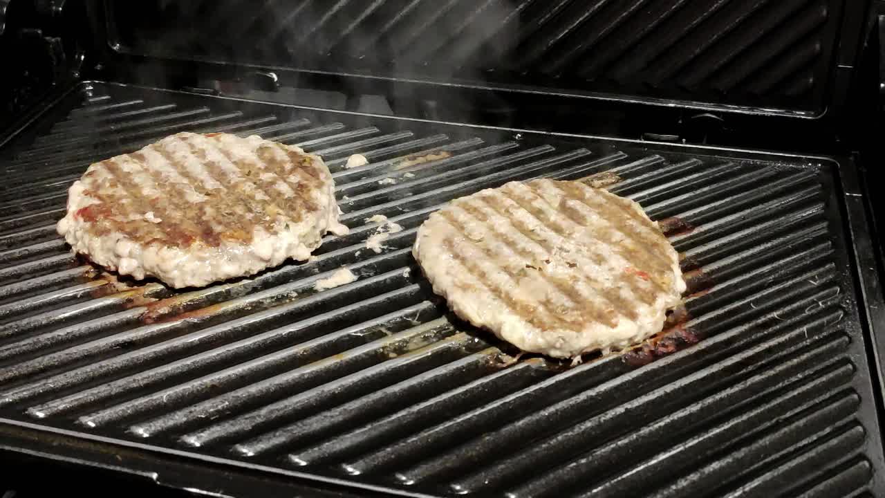 two homemade hamburgers cooking on a black grill