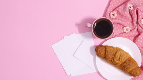 fresh croissant cup of coffee and paper from envelope appear on pastel pink background. stop motion