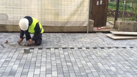 Trabajador-Del-Ajuntament-Público-De-Barcelona-Con-Martillo,-Casco-Y-Chaqueta-Amarilla-Colocando-Un-Bloque-Cuadrado-De-Hormigón-En-Una-Calle-Peatonal-O-Acera-En-Construcción