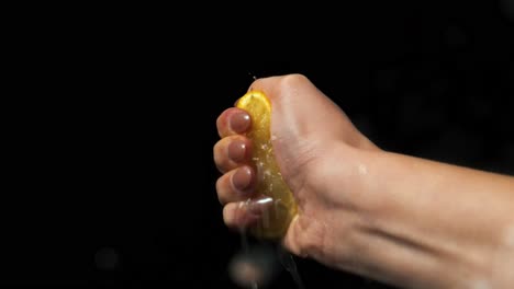 Static-slow-motion-shot-of-a-woman's-hand-with-a-lemon-being-squeezed-in-her-hand-while-the-lemon-juice-is-running-out-in-front-of-black-background