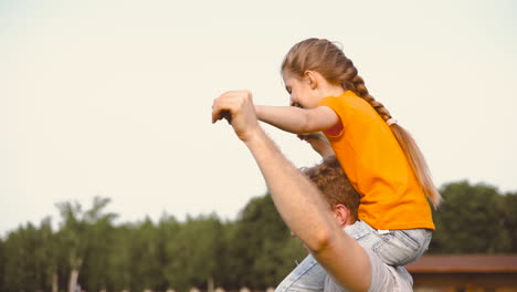 joyful father carrying his happy daughter on shoulders and spinning around in a park 1