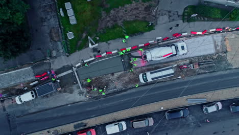 vista aérea de arriba hacia abajo de varios trabajadores que refuerzan el pavimento de un puente en un gran sitio de construcción con camiones