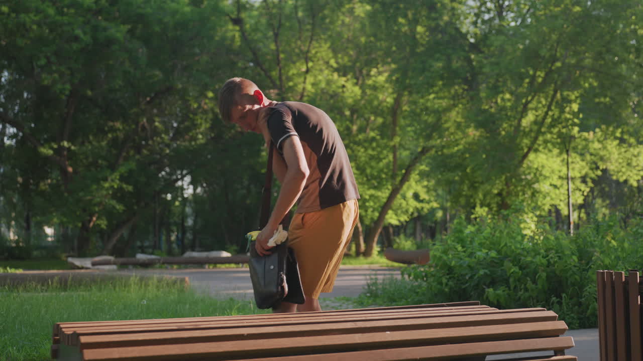 Cleanliness In Progress, Man Sanitizing Park Bench Carefully, Person Disinfects Bench With Precise Movements, Man Diligently Sanitizes Bench Using Careful Strokes In Peaceful Outdoor Setting