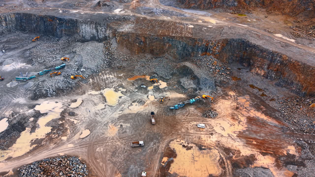 Work in a stone quarry during the day. Construction vehicles move around a stone quarry. Workers manage the equipment and rocks at the site