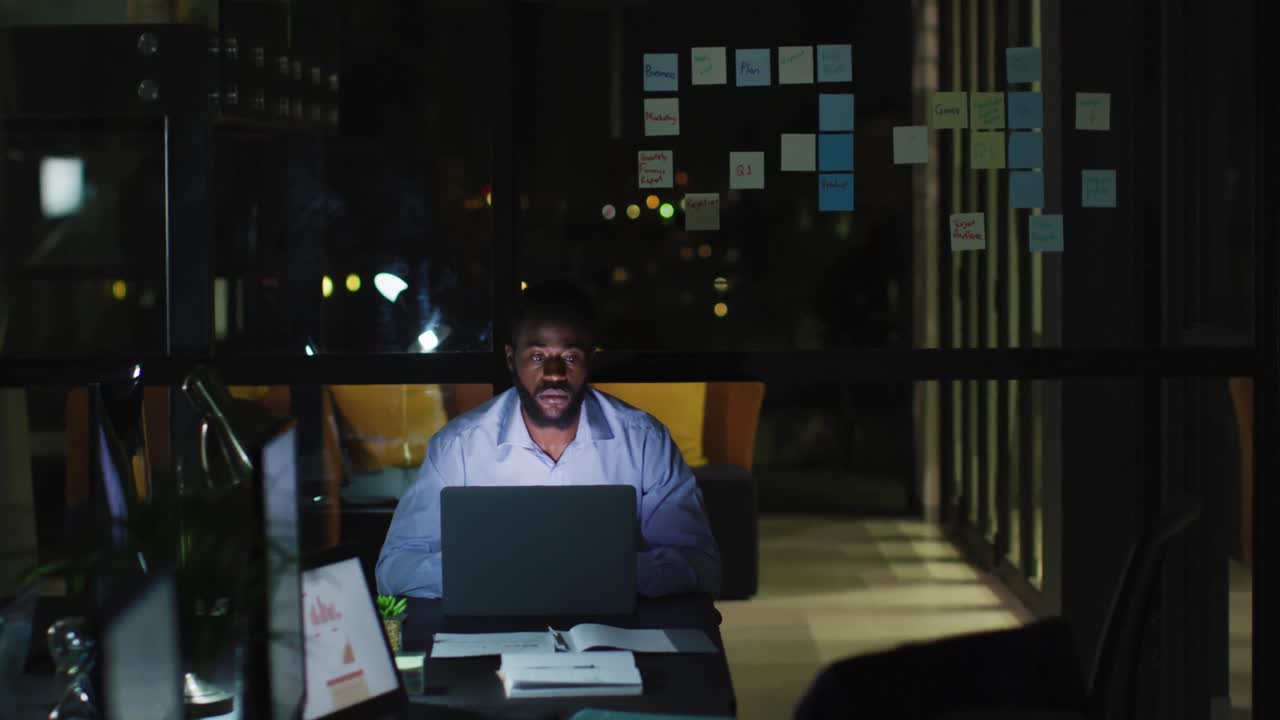 vídeo de um empresário afro-americano cansado na mesa usando laptop, trabalhando sozinho à noite no escritório