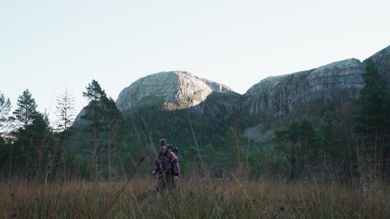 Turgåer med hunden sin går på den gresskledde stien til campingplassen med fjellkjede.
