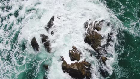 Static-aerial-top-down-of-heavy-waves-crashing-against-rock-formation-in-ocean,-Riversdale,-New-Zealand