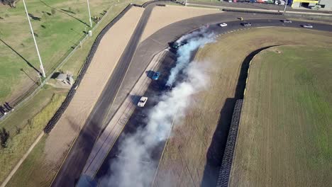 Coches-De-Carreras-A-La-Deriva-Con-Humo-Blanco-De-La-Quema-De-Neumáticos-En-La-Pista-De-Carreras---Toma-Aérea