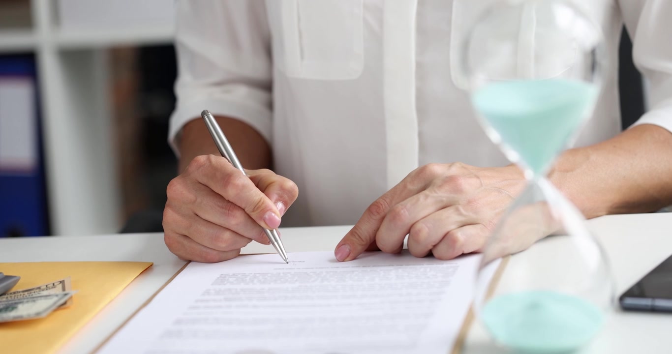 Woman holds silver pen and actively signs document at desk