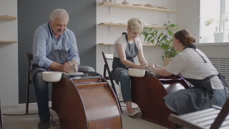 a female potter's wheel sculpting teacher explains how to work and teaches an elderly woman to work with clay and make mugs and jugs. master class for pensioners. pottery courses