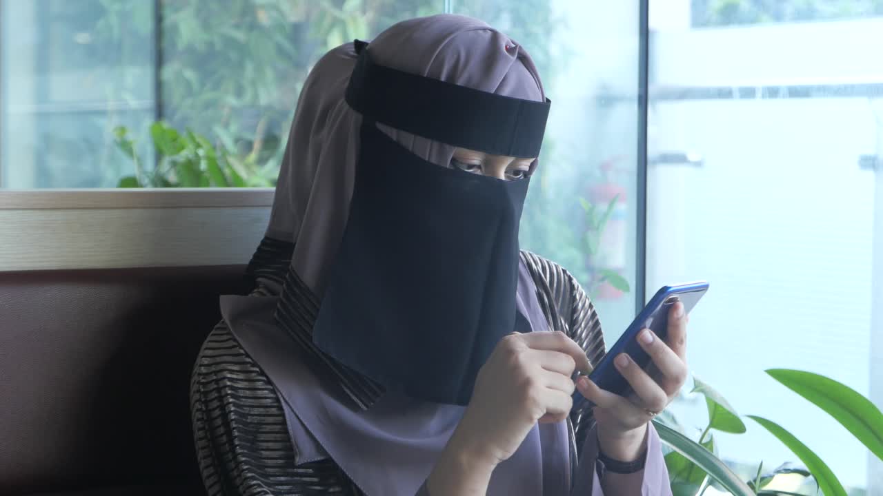 Wanita Muslimah menggunakan ponsel pintar di kafe