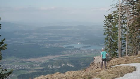 running down to a tree stump to celebrate as a hiker looks over austria and the city of villach