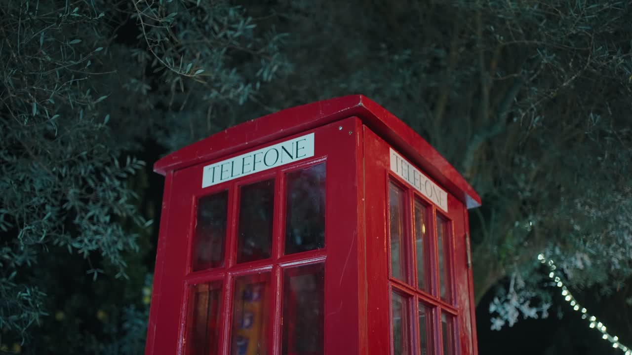 밝은 빨간색 전화 부스는 배경에 나무와 함께 밤에 야외에 조명