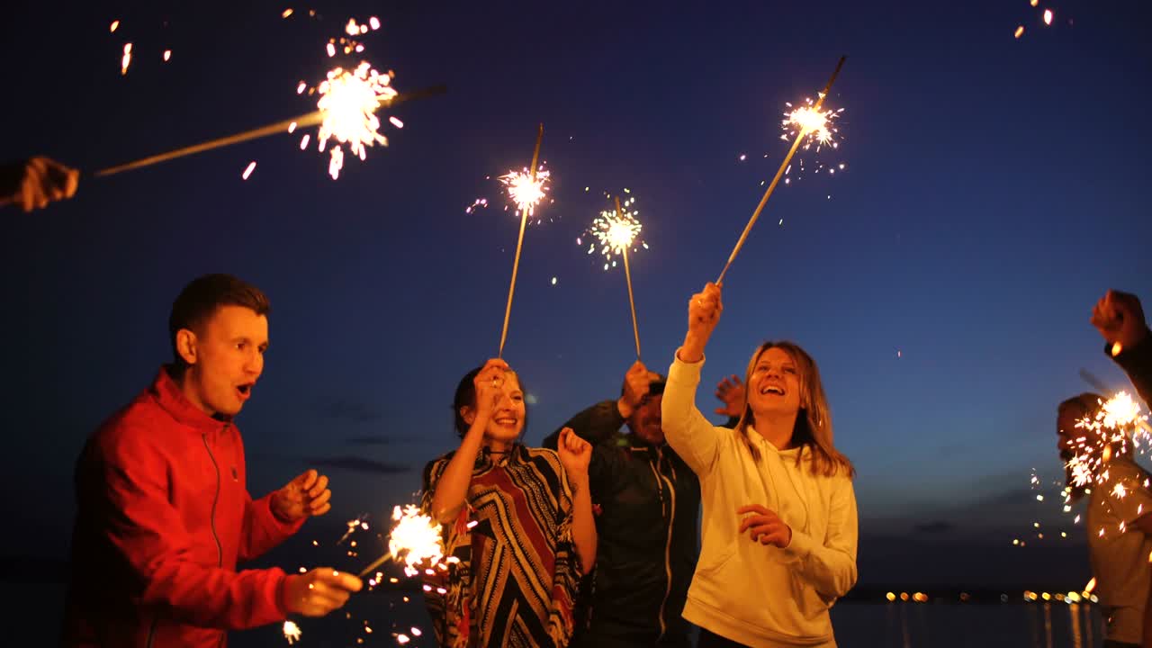 Group of young friends having a beach party. Friends dancing and celebrating with sparklers in twilight sunset