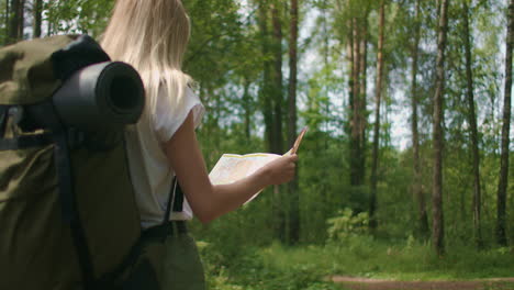 a young woman with a map walks through the forest traveling with a backpack in slow motion