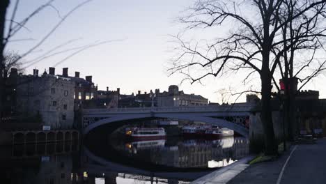Wide-angle-reveal-of-calm-and-reflective-river-and-historic-bridge-over-the-water-at-sunrise