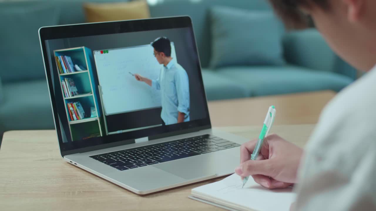 Close Up Of Asian Man Student Look At Teacher In Computer Screen And Write In The Notebook While Studying Online At Home