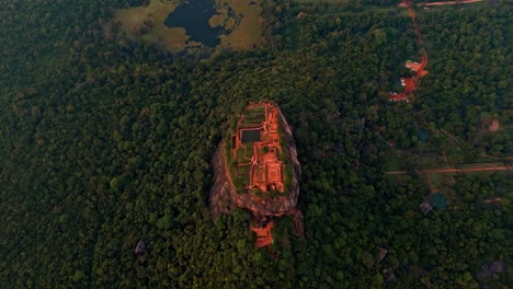 top-down vertical drone shot over sigiriya rock fortress at sunrise, revealing the ancient symmetrical layout of the ruins surrounded by dense jungle and glowing morning mist.