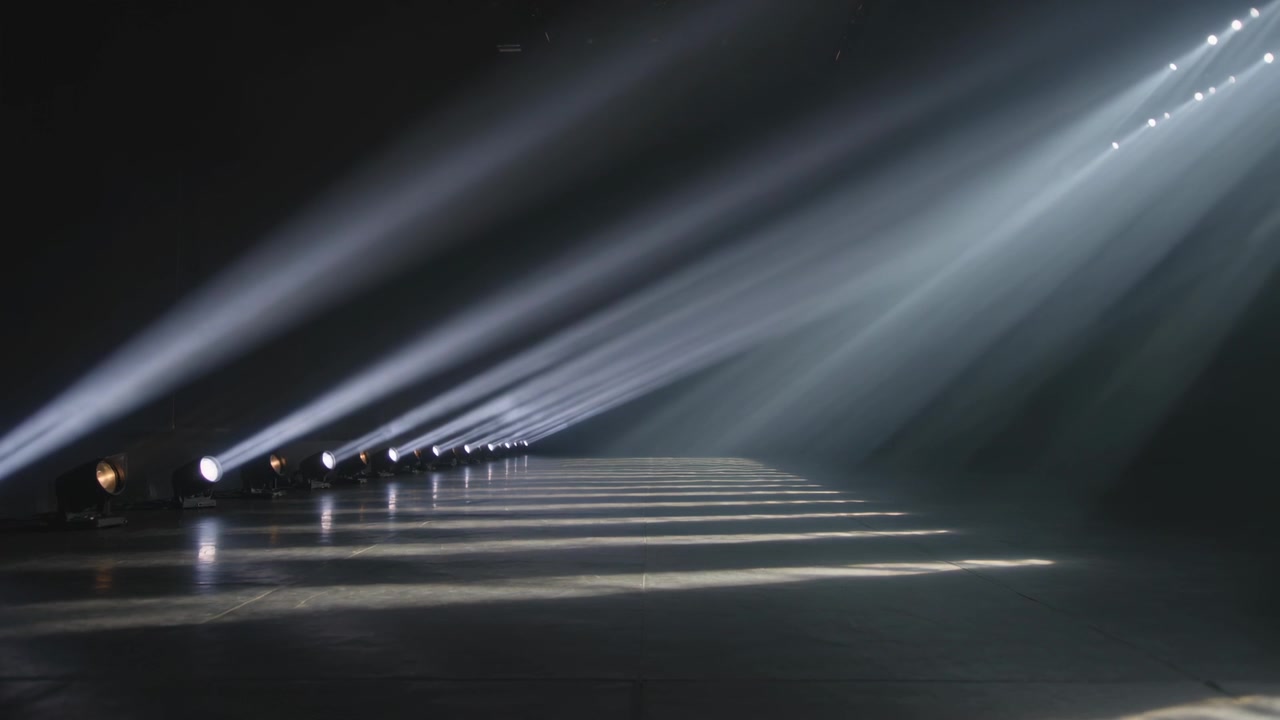 Switching on spotlight row projecting cool beams across polished floor through haze for stage test