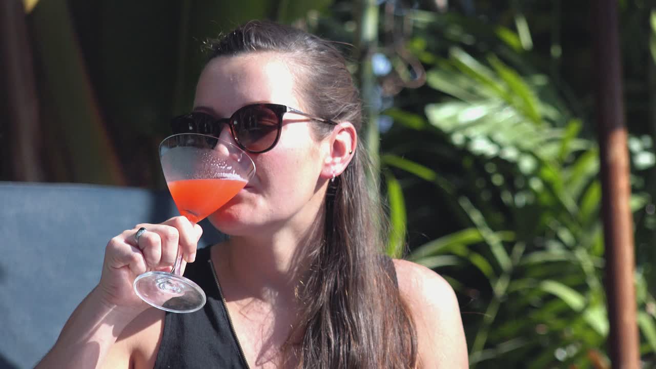 Primo piano di una giovane donna con occhiali da sole che si gode un cocktail in un hotel tropicale