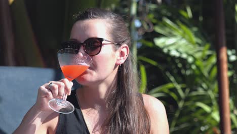 primer plano de una joven con gafas de sol disfrutando de un cóctel en un hotel tropical