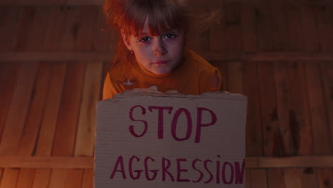 afraid homeless toddler girl sitting holding inscription stop aggression, hiding from bombing attack