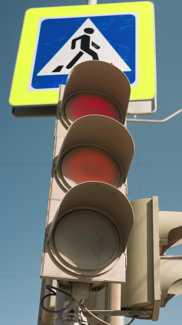 vista cercana de un semáforo que cambia de rojo a verde, situado cerca de una señal de cruce de peatones, captura elementos de la calle urbana y la transición de las señales de tráfico