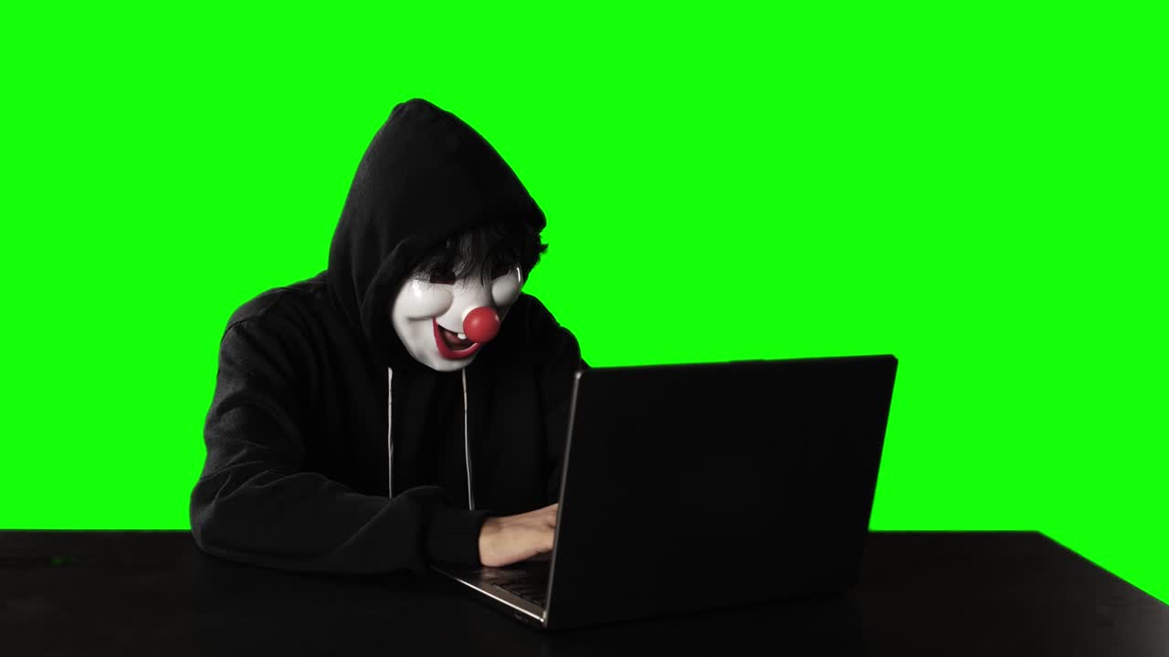 hombre usa una máscara de payaso mientras hackea con una computadora portátil