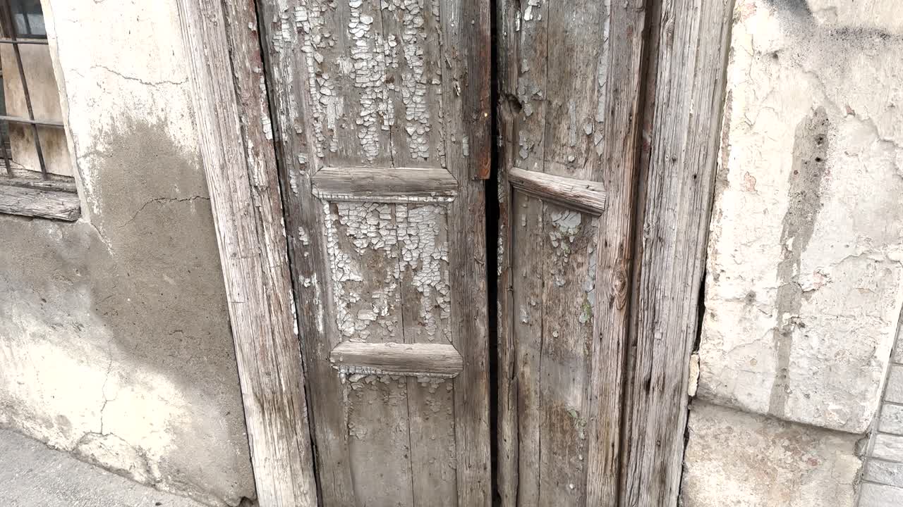 Close-up of a distressed wooden door with flaking paint and visible decay on aged stone wall