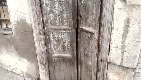 close-up of a distressed wooden door with flaking paint and visible decay on aged stone wall