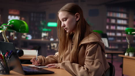 vertical video college student working on laptop under green lamp in a quiet setting