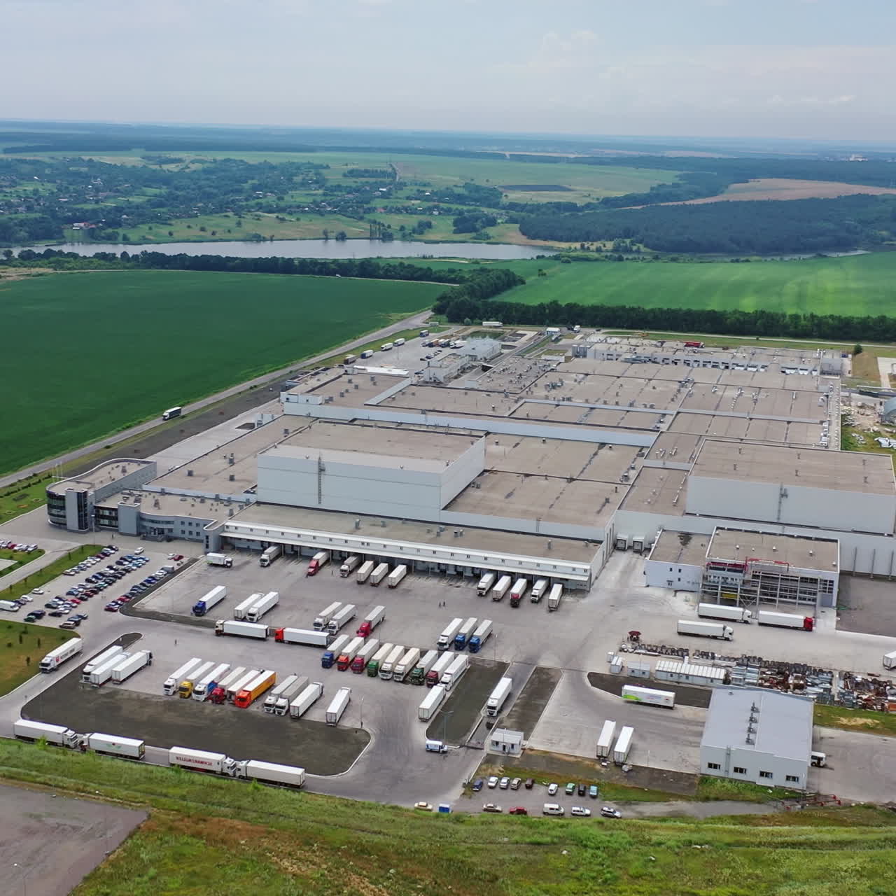 Aerial footage of a large industrial complex. Many white trucks and different cars are on parking place near the large manufacturing plant. Aerial view.
