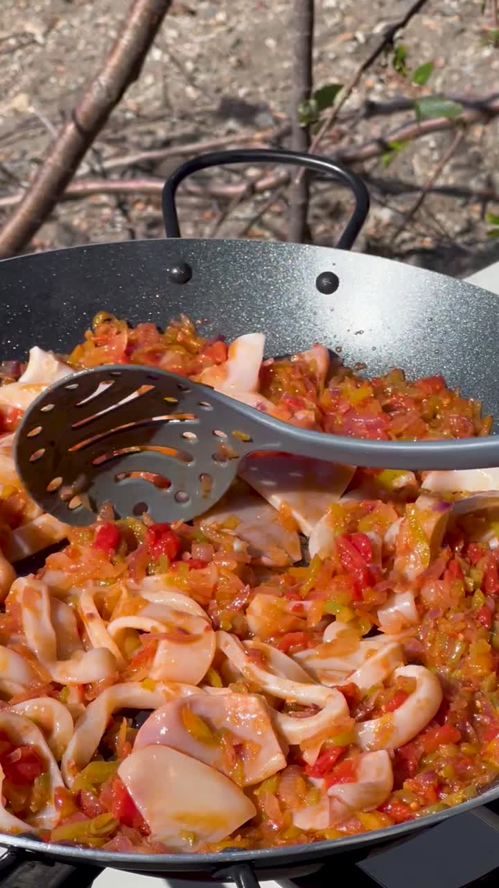 Cooking Paella outdoors with colorful vegetables and noodles in a skillet