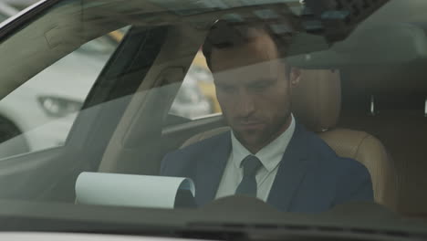 businessman looking through papers in front car seat