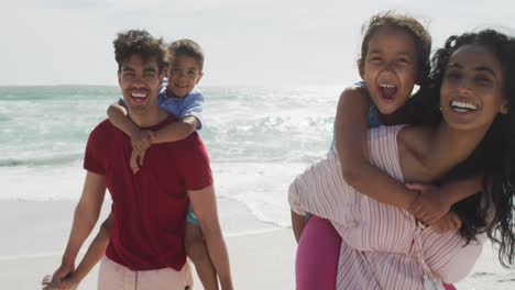 padres hispanos felices llevando a sus hijos en una mochila en la playa