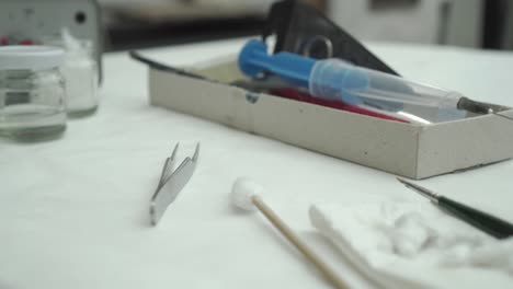 도구가 가득한 복원기 테이블 - 페인트 브러시, 주사바늘, 용액이 담긴 용기, 면 누에고치