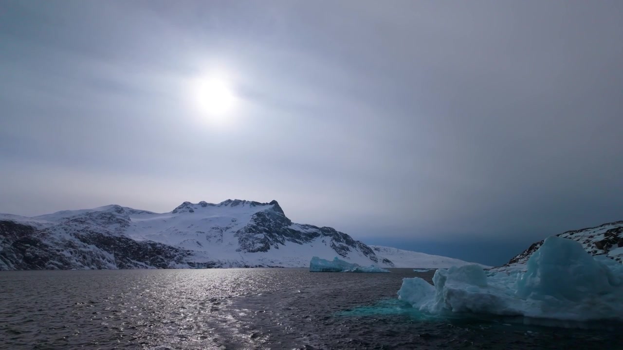 Icebergs flutuam em água fria com montanhas nevadas sob a luz solar ártica brilhante