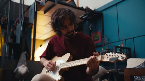 a brunette guy with patlaty hair in a red t-shirt plays the electric guitar at home. video filmed in high quality