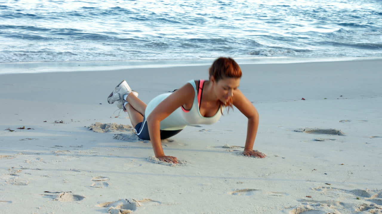 Fit brunette doing press ups on the beach