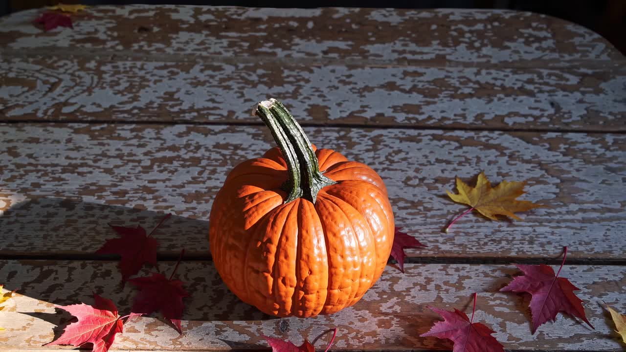 A rustic autumn scene with a pumpkin on a weathered table, surrounded by fallen leaves