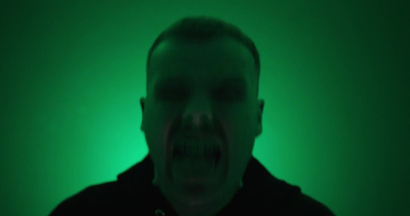 Uomo che scuote la testa e tira fuori la lingua sotto un'illuminazione verde drammatica. Concetto di follia, caos, emozione estrema, pazzia e comportamento selvaggio.