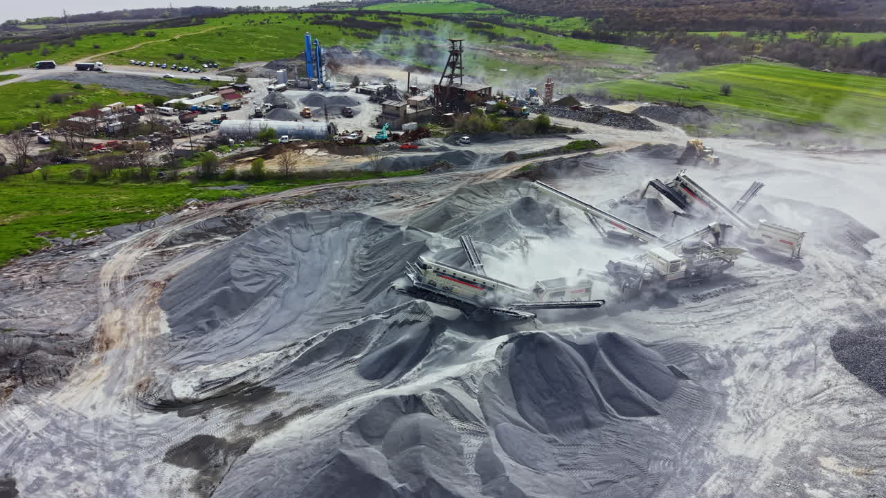 Operasi tambang granit yang menunjukkan peralatan, tumpukan material, dan lanskap pada siang hari di lokasi penambangan.