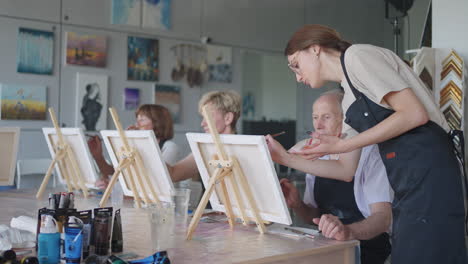 high angle view of cheerful senior friends painting on canvas. senior woman smiling while drawing with the group. seniors attending painting class together. senior men having fun painting in art class