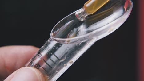 man takes liquid from spoon with pipette on dark background