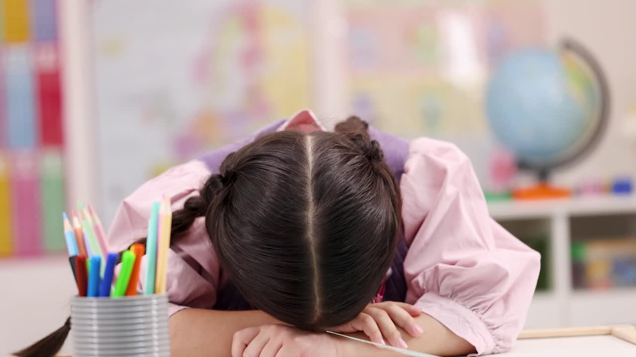 Ragazza asiatica in classe, stanca e annoiata, con la testa appoggiata al banco, illuminazione intensa