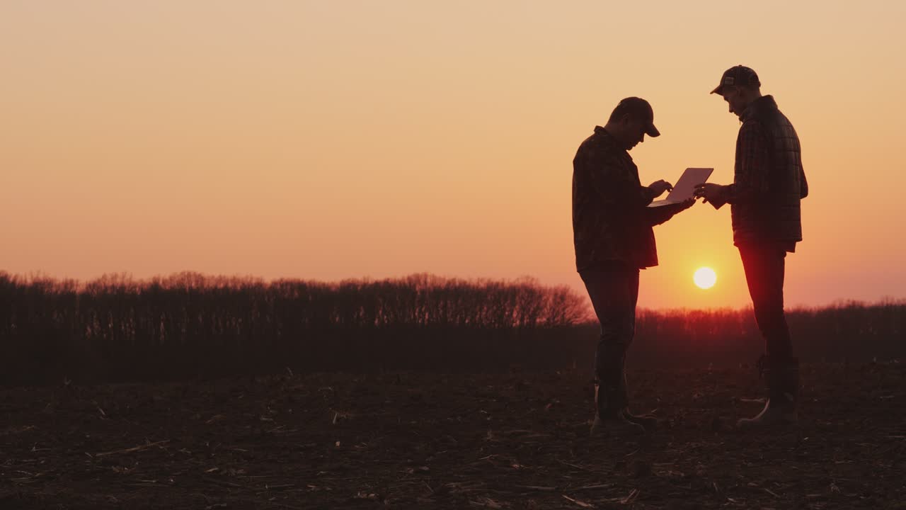 Two male farmers working in the field, using a laptop and tablet