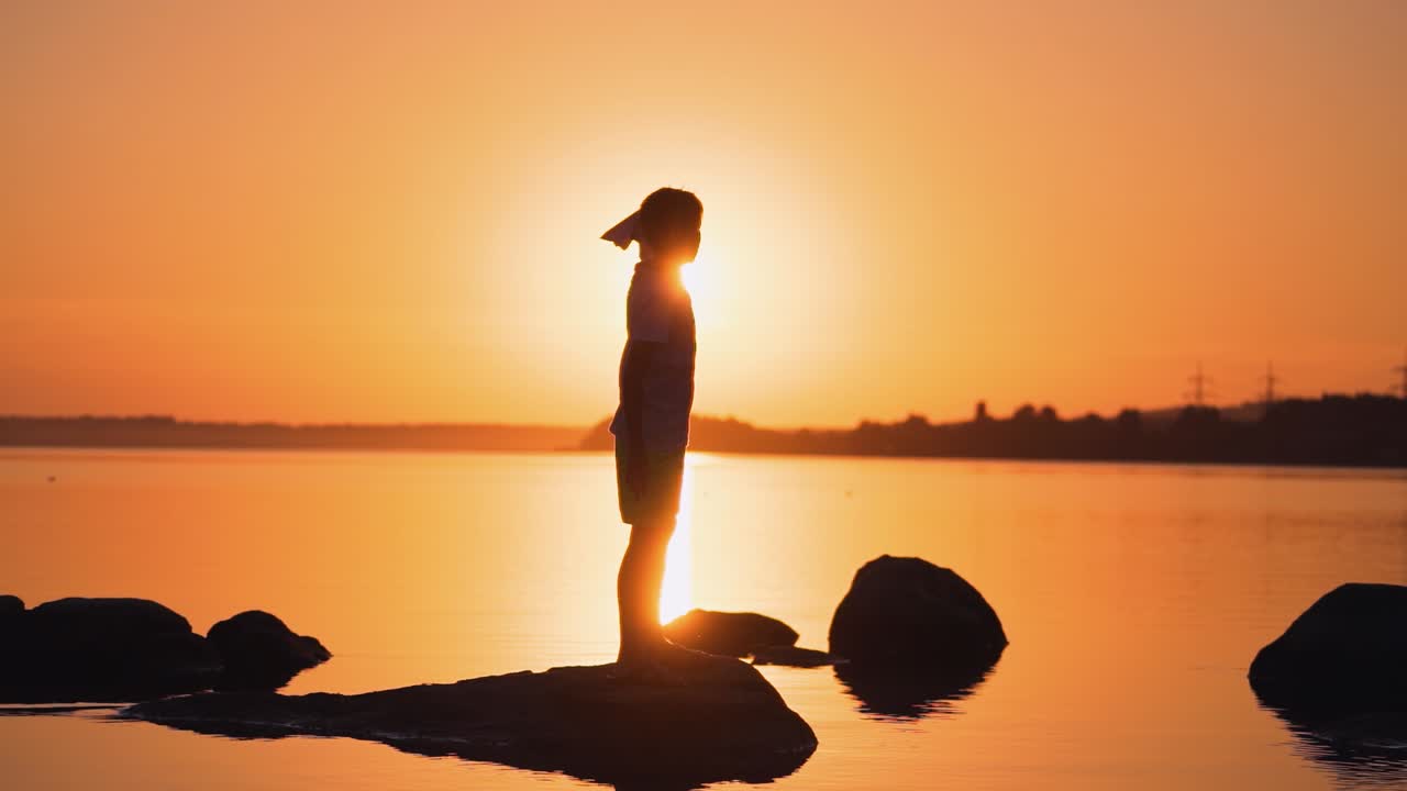 Boy resting near the water. Silhouette of cute young boy standing on stone holding small paper plane in hands