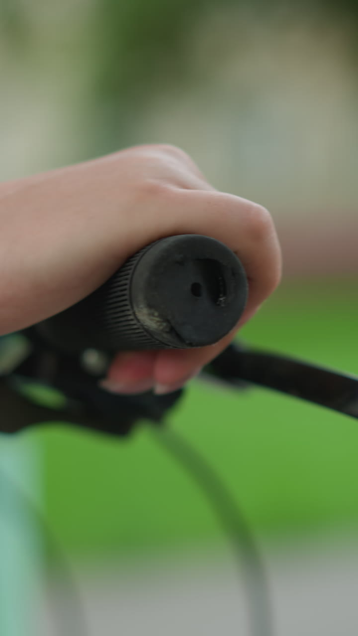 primer plano de la mano de la persona agarrando el manillar de la bicicleta mientras se pasea por el camino del parque con una bolsa de color menta visible, en contra de un fondo de vegetación borrosa
